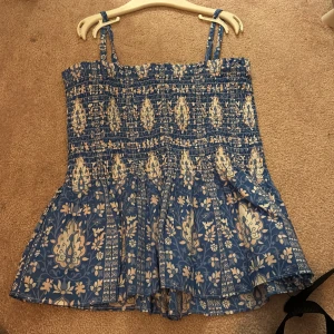 Blå blommig kortklänning Gina Tricot - Supersöt topp från Gina Tricot med smala axelband och smock upptill. Toppen är blå med rosa å vit blommigt mönster och har en luftig, volangig nederdel. Perfekt för sommarens varma dagar och har en riktigt chill vibe. Man kan även ta bort banden så det blir en tube topp! 