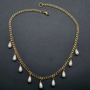 Guldhalsband med droppformade pärlor - Snyggt halsband i guldfärgad kedja med hängande droppformade vita pärlor. Kedjan har en klassisk länkdesign och pärlorna ger en elegant och trendig vibe. Perfekt för dig som vill sticka ut med en unik accessoar.