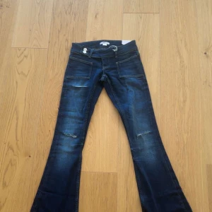 Blå bootcut jeans från Gina Tricot XXS - Snygga blå bootcut jeans från Gina Tricot i storlek XXS. Jeansen har låg midja, slitna detaljer på benen och stora fickor fram. Tillverkade i stretchig bomullsdenim för en bekväm passform. Perfekta för dig som gillar en retro vibe.