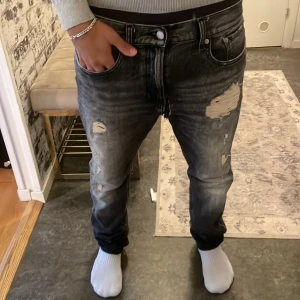 Svarta slitna jeans från Calvin Klein SLIM - Säljer ett par svarta jeans från Calvin Klein med coola slitningar och tvättad look. Jeansen har normal passform, klassisk femficksdesign och tydlig logga bak i midjan. Perfekta för dig som gillar en edgy streetstil. 