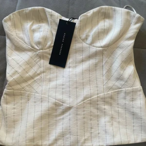 Vit randig korsettopp från Bershka - Supersnygg vit korsettopp från Bershka med tunna svarta ränder och markerade kupor. Stor i storlek så passar en S. Toppen har snörning i ryggen för perfekt passform och är axelbandslös. Materialet känns lite strukturerat och ger en cool vibe till outfiten. Oanvänd med lappen kvar❤️
