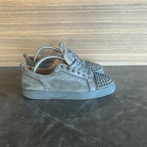 Grå mocka sneakers med nitar Louboutin - Säljer ett par feta loubs som är i ganska bra skick då de har nån liten effekt på spikarna då färgen har gått av lite men annars inget .Allt og med kommer som box påse och sånt .Hör av er vid minste fundering!