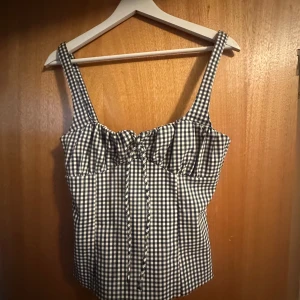 Rutig korsettopp med snörning S - Supersöt korsettopp i blåvitt rutigt mönster med breda axelband och snygg snörning framtill. Toppen har en feminin form och är perfekt för att lyfta din stil. Materialet känns lätt och somrigt, och den croppade modellen ger en trendig vibe.