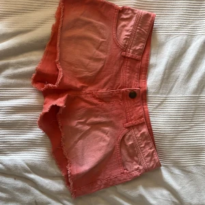 Korallrosa jeansshorts - Snygga korallrosa jeansshorts med fransig, rå kant och klassiska fickor både fram och bak. Modellen har lowwaist och bälteshällor, perfekt för en chill sommarlook. Materialet är jeans och färgen är riktigt poppig rosa som sticker ut.