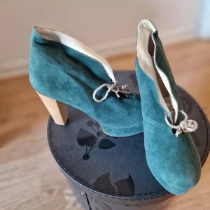 Gröna mocka stövletter med klack - Unika gröna stövletter i mjuk mocka med träfärgad klack. Skorna har rund tå, snörning framtill och en snygg plattform som ger extra höjd. Perfekt för dig som vill sticka ut med en cool färg och retrovibe. Använd vid 1 tillfälle.