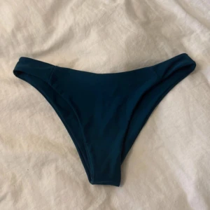 Mörkblå/grön bikiniunderdel - Snygg mörkblå/grön bikiniunderdel med klassisk, enkel design och låg midja. Materialet är mjukt och stretchigt syntet som sitter skönt mot huden. Perfekt för strandhäng eller poolen, och färgen ger en cool vibe till din badoutfit.