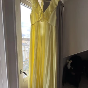 Ljusgul långklänning från Zara - Säljer en drömmig ljusgul långklänning från Zara med plisserade volanger längs v-ringningen och axlarna. Klänningen har ett flowigt fall och är ärmlös med knyt i nacken🥰