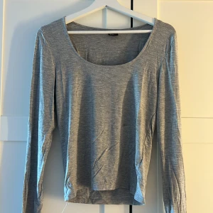 Grå långärmad topp med rund hals - En basic grå långärmad topp från Gina Tricot med rundad, djup halsringning. Tunt och mjukt material som känns skönt mot huden. Perfekt att styla med jeans eller kjol för en enkel och clean look.