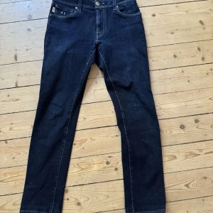 Mörkblå jeans från Tramarossa - Snygga mörkblå jeans från Tramarossa med klassisk femficksdesign och detaljer som AE-bokstäver på myntfickan. Jeansen har raka ben, kontrastsömmar och metallknappar. Perfekta för dig som gillar stilrena och tidlösa jeans.
