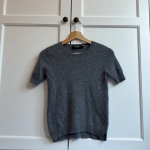 Grå kashmirtröja från Lisa Yang - Superskön grå tröja från Lisa Yang i 100% kashmir. Rund halsringning och korta ärmar ger en clean och chill look. Perfekt för dig som gillar mjuka material och enkel stil. Ribbstickade detaljer vid hals, ärmslut och nederkant.