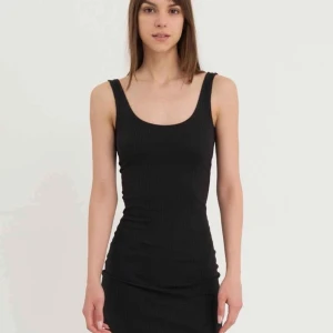 Svart ribbad ärmlös kortklänning - Säljer en svart klänning med ärmlös design och rundad halsringning. Klänningen är kort och har en slim passform som framhäver figuren. Perfekt för dig som gillar enkel och stilren look. Endast provad!