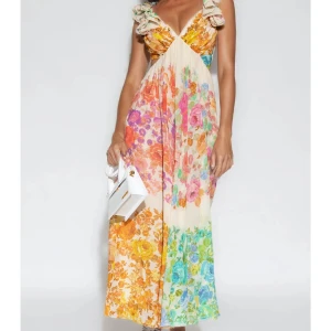 Blommig långklänning från Mior Paris - Superfin långklänning från Mior Paris med färgglatt blommönster i orange, rosa, blått och grönt på ljus botten. Klänningen har volangärmar, v-ringning, öppen rygg och knyt i ryggen. Aldrig använd med lappen kvar!!!