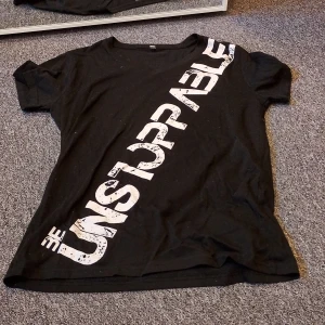 Svart t-shirt med tryck "Be Unstoppable" - Svart t-shirt i storlek M med coolt vitt tryck diagonalt över framsidan där det står "Be Unstoppable". Klassisk rund hals och korta ärmar. Materialet känns som mjuk bomull, perfekt för en chill och sportig look. Kan tvättas innan jag skickar det om du vill😄