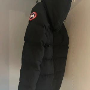 Canada Goose macmillan parka  - Säljer en svart dunjacka från Canada Goose med klassisk patch på ärmen och huva. Jackan är fylld med dun och fjäder, har en clean look och är perfekt för kalla vinterdagar. Yttermaterialet är polyester och bomull, fodret är polyamid.
