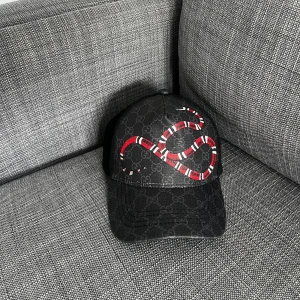 Gucci keps  - Svart keps från Gucci med klassiskt GG-monogram och en röd-vit orm broderad på framsidan. Justerbar rem baktill med grönt och rött band. Tillverkad i bomull och polyester, levereras med originalförpackning. Perfekt för dig som vill sticka ut med lyxig streetstyle.