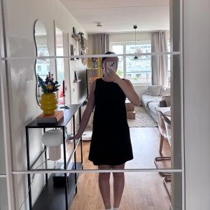 Svart ärmlös kortklänning - Enkel och stilren svart kortklänning med rund halsringning och ärmlös design. Klänningen har en rak passform och stängs med dragkedja i ryggen. Perfekt för dig som gillar minimalistisk stil.