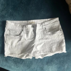 Vita jeansshorts med fransig kant - Snygga vita jeansshorts från True Religion med klassisk femficksdesign och fransig kant nertill. Shortsen har låg midja, silverfärgade nitar och dragkedja. Perfekta för sommaren och ger en fräsch look till alla outfits.