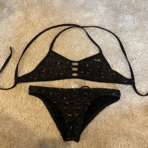Svart och gul bikini från TYR, S - Snygg bikini från TYR i svart med geometriskt mönster i gult.. Både över- och underdel har TYR-logga. Tillverkad i stretchig polyester och spandex. Använd bara en gång🫶