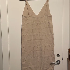 Beige stickad klänning!  - Superfin beige stickad klänning med geometriskt mönster och v-ringning. Klänningen är ärmlös med breda axelband och har en kort längd. Perfekt för dig som gillar en chill och stilren look med lite edge.