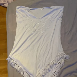 Två fransiga toppar med paljetter - Säljer två snygga toppar i vitt och rosa med v-ringning och dekorativa paljetter framtill. Båda har fransar längs nederkanten och är ärmlösa med en asymmetrisk, spetsig form nedtill. Perfekta för sommarens festivaler eller strandhäng!