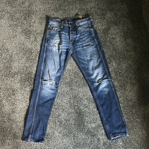 Jack & Jones blå jeans 28/30 - Säljer ett par blå Original jeans från Jack & Jones i storlek 28/30. Jeansen har skinny passform, slitningar och snyggt tvättad look. Klassisk femficksmodell med dragkedja och detaljerade sömmar. Perfekta för dig som gillar en smal siluett.