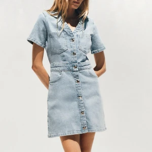 Ljusblå jeansklänning med knappar - Snygg ljusblå jeansklänning med kort ärm, v-ringning och knappar hela vägen framtill. Klänningen har två bröstfickor, markerad midja och klassiska jeanssömmar. Perfekt för en cool och avslappnad look. Från Zara!