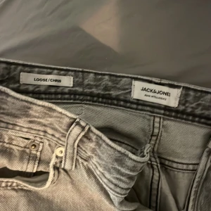 Grå loose fit jeans Jack & Jones - Säljer ett par grå  jeans från Jack & Jones, modell Chris.t Jeansen har klassisk femficksdesign, raka ben och snyggt tvättad finish. Perfekta för dig som gillar en avslappnad och trendig look. 