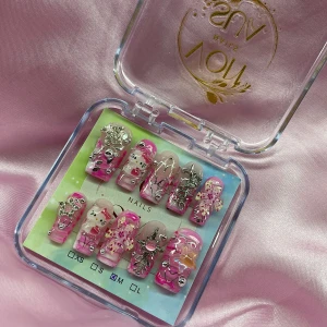 LilZap (M);Medium Square - Ett set med handgjorda gelé press-on naglar i storlek M: 16 mm, 12 mm, 12,5 mm, 11,5 mm, 10 mm. Naglarna har rosa och nude bas med 3D-dekorationer som Hello Kitty, stjärnor, hjärtan, blommor och silvriga detaljer. Mix av glittriga stenar och metallic effekter för en extra poppig look.