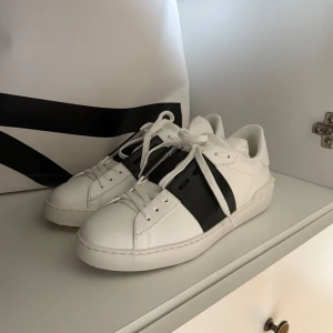 Valentino Garavani Open Sneakers - Snygga Valentino Garavani Open sneakers i vitt skinn med en bred svart läderdetalj över mitten. Klassisk rund tå, vita snören och diskreta nitar på hälen. Kommer med originalkartong, dustbag och extra skosnören. Storlek 40, aldrig använda och i super fint skick. 5500 kr + frakt! Vid fler frågor, etc skriv privat ☀️🙌🏼🙏🏼🏄🏽‍♀️🩷