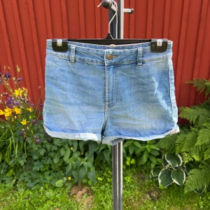 Blå jeansshorts från H&M Devided - Blå jeansshorts från H&M Divided. Shortsen har normal passform och hög midja. Knapp och dragkedja framtill. Storlek 36/38