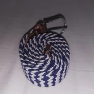 Blåvitt flätat bälte  - Snyggt bälte med blåvitt sicksackmönster och detaljer i brunt skinn vid spännet. 