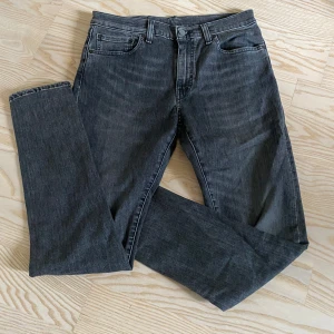 Levi's 501 svarta jeans W32 L34 - Snygga svarta Levi's 501 jeans i klassisk rak modell. Jeansen har fem fickor, knappgylf och den ikoniska röda Levi's-taggen bak. Perfekt tvättad svart färg som ger en cool och avslappnad vibe. Passar dig som gillar tidlös stil och streetwear.
