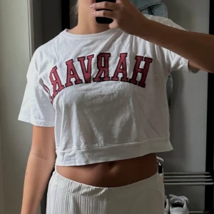 Vit croppad t-shirt - Säljer en vit croppad t-shirt från Zara med stora röda bokstäver framtill ”HARVARD”. T-shirten har korta ärmar, rund halsringning och är gjord i mjuk bomull. 