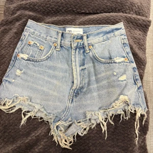 Blåa  jeansshorts från Zara - Snygga ljusblå jeansshorts från Zara, fransiga kanter. Shortsen har slitna detaljer både fram och bak, klassiska fem fickor och dragkedja med knapp. Perfekta för en chill sommarlook.