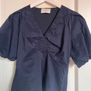 Mörkblå topp Neo Noir - mörkblå blus/topp från Neo Noir med puffiga korta ärmar och v-ringning med rynkade detaljer framtill. Använd max 1 gång💕🌸 strl 34 men passar även 36
