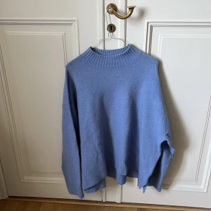 Blå stickad tröja från Uniqlo XL - Mysig blå stickad tröja från Uniqlo i storlek XL. Tröjan har en relaxed fit med ribbade muddar och hög hals. Perfekt för lager-på-lager och chill dagar. Enkel att matcha med jeans eller kjol för en avslappnad look.