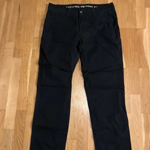 Mörkblå raka chinos med knappar från Pelle P - Svarta byxor med raka ben och snygga detaljer som dubbla knappar i midjan och bakfickor med knappstängning. Byxorna har en klassisk look och är tillverkade i ett mjukt bomullsmaterial med lite stretch. Perfekta för en clean och stilren outfit.