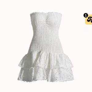 Vit klänning från Design by Amor - Supersöt vit kort klänning med smockad överdel och axelbandslös design. Kjolen har två lager volanger med broderade hål för en romantisk vibe. Perfekt för sommarens alla tillfällen och ger en fräsch look.                          Köpt för 550kr 
