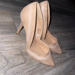Beige pumps - Snygga beige pumps från Atmosphere med spetsig tå och hög klack. Skorna är i mocka med detaljer i blankt syntetmaterial som ger en stilren look. Perfekta för dig som vill ha en klassisk och trendig sko med lite extra edge.