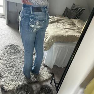 Lågmidjade jeans med broderade fickor - Ljusblå jeans från Sky med snygga broderade kors och bling på bakfickorna. Modellen har låg midja och raka ben med en lätt bootcut-vibe. Jeansen är i klassisk denim och har coola detaljer som kontrastsömmar och slitningar. Perfekta för dig som vill sticka ut.