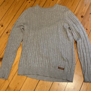 Grå stickad tröja från Bondelid M - Snygg grå stickad tröja från Bondelid i storlek M. Tröjan har ett klassiskt kabelstickat mönster, rund halsringning och ribbade muddar vid ärmslut och nederkant. Perfekt för lager-på-lager.