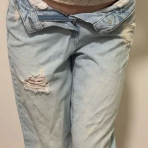 Ljusblå ripped jeans Lågmidjade - Säljer ett par ljusblå jeans med slitna detaljer och stora hål vid knäna. Jeansen har fransiga benslut och en relaxed, loose fit.Låg midjade. Low waist jeans med slitningar.  Midja: 31cm  Gylf: 10cm  Innerben: 63cm  Ytterben: 92cm   Storlek: XXS (men skulle mer säga XS-S)