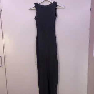 Grå ribbad långklänning H&M Divided - Säljer en grå ribbad långklänning från H&M Divided. Klänningen är ärmlös, har rund halsringning och en snygg slits bak. Den är figurnära och stretchig, perfekt för dig som gillar en enkel men stilren look.