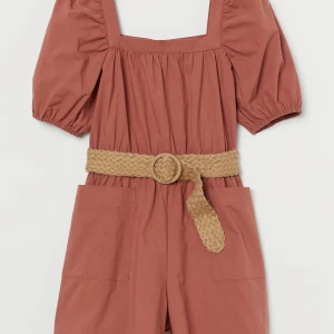 Rostbruna byxklänning med bälte och fickor - Snygga rostbruna shorts i bomull med hög midja och breda ben. De har stora, praktiska fickor framtill och ett flätat beige bälte med rund spänne som ger en chill vibe. Perfekta för varma dagar och enkel att styla med en crop top eller t-shirt.