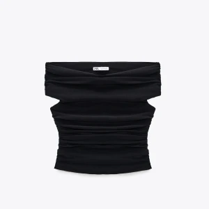 Svart bandeau tubtopp från Zara - Svart bandeau tubtopp från Zara med snygga rynkade detaljer. Toppen är axelbandslös och sitter tight runt kroppen, perfekt för att skapa en cool och trendig look. Enkel att matcha med både jeans och kjol.