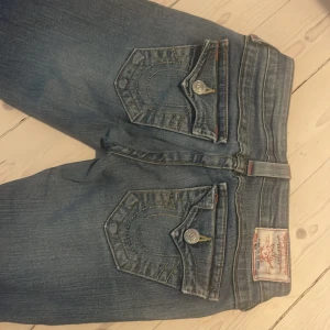 True Religion bootcut jeans low waist  - Snygga blå jeans från True Religion med bootcut passform och slitna detaljer nertill. Klassiska kontrastsömmar, stora fickor med lock och silverfärgade knappar. Bra skick förutom slitningarna längst ner 🩷🩷