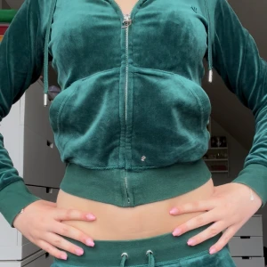 Grön velour set Juicy Couture - Mörkgrön velour set från Juicy Couture med dragkedja framtill, huva och ribbade muddar. Jackan är croppad och har en sportig vibe med snörning i matchande byxor.  Hela sättet köptes föf 2300kr. Går att köpa separat ifall man vill!💕pris kan diskuteras. Har en liten rosa fläck på tröjan men märks knappast!
