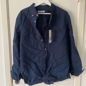 Mörkblå skjorta från Zara i linne - Snygg mörkblå skjorta från Zara i luftig linnemix. Klassisk krage, bröstficka och knappar framtill. Perfekt för dig som gillar en enkel och stilren look. Skjortan har långa ärmar och en avslappnad passform.