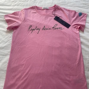 Rosa t-shirt från Replay - Snygg rosa t-shirt från Replay med glittrig text 'Replay denim Power' på bröstet. Klassisk rund halsringning och korta ärmar. Skön och mjuk bomullskvalitet, perfekt för en chill och trendig look.