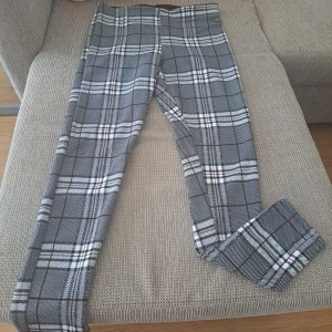 Grå rutiga kostymbyxor - Snygga grå kostymbyxor med klassiskt rutigt mönster i svart och vitt. Byxorna har en rak passform och är perfekta för en stilren look. De är tillverkade i ett mjukt material som känns bekvämt hela dagen.